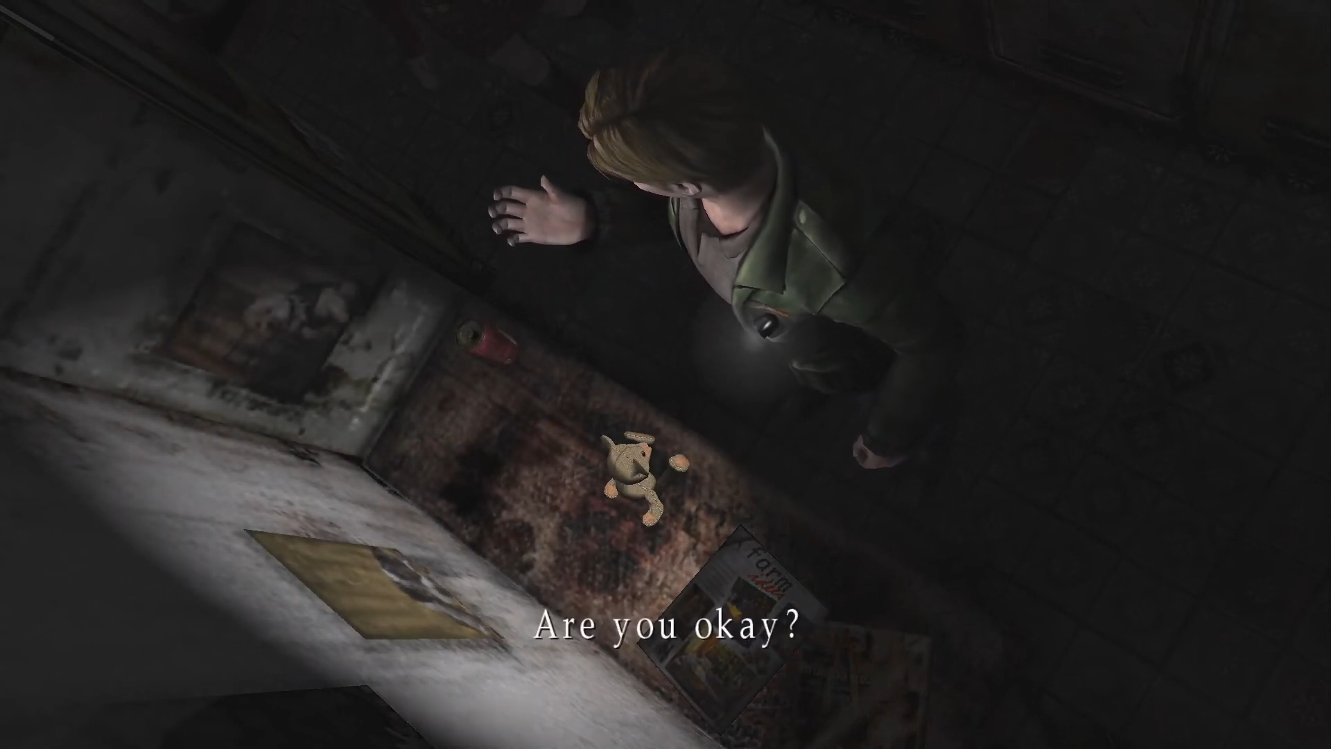 a screenshot from the original 2001 release of cult horror videogame silent hill 2, wherein the protagonist james sunderland holds his hand up in confusion before a tattered bear doll sitting on a desk in a dark room, while another character, maria, asks 'are you okay?' as she comes to investigate